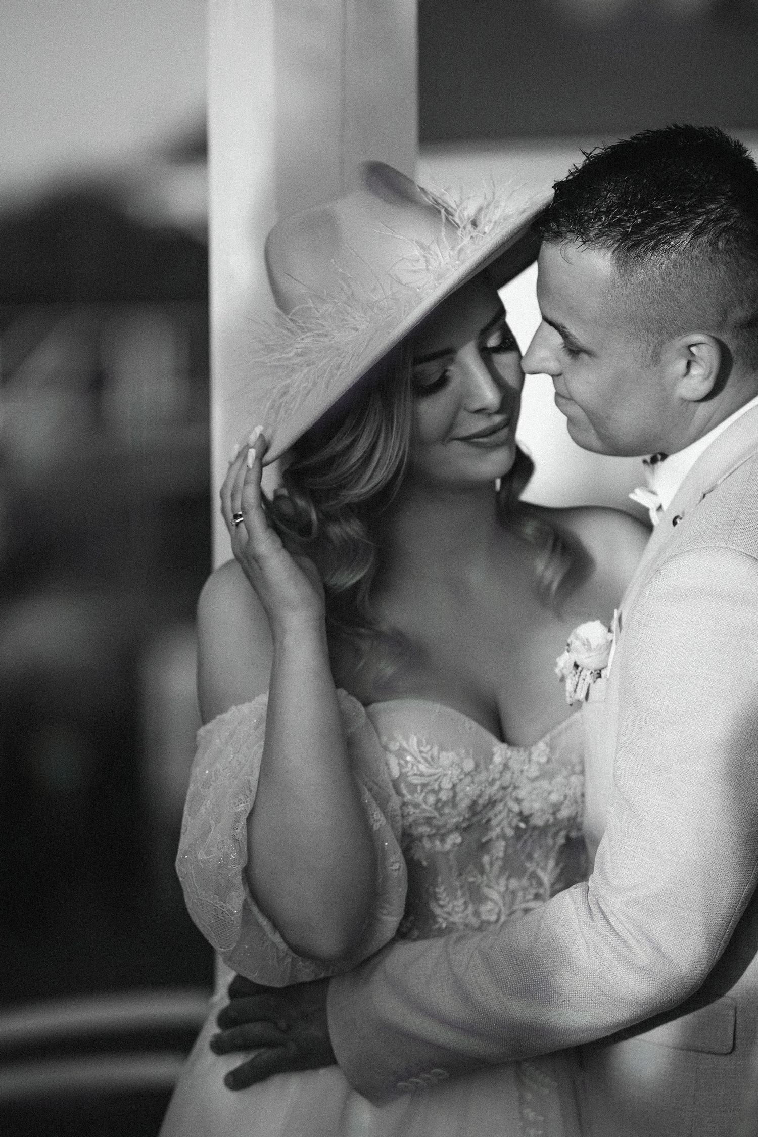 Intimate black and white portrait of wedding couple sharing romantic moment against wall.