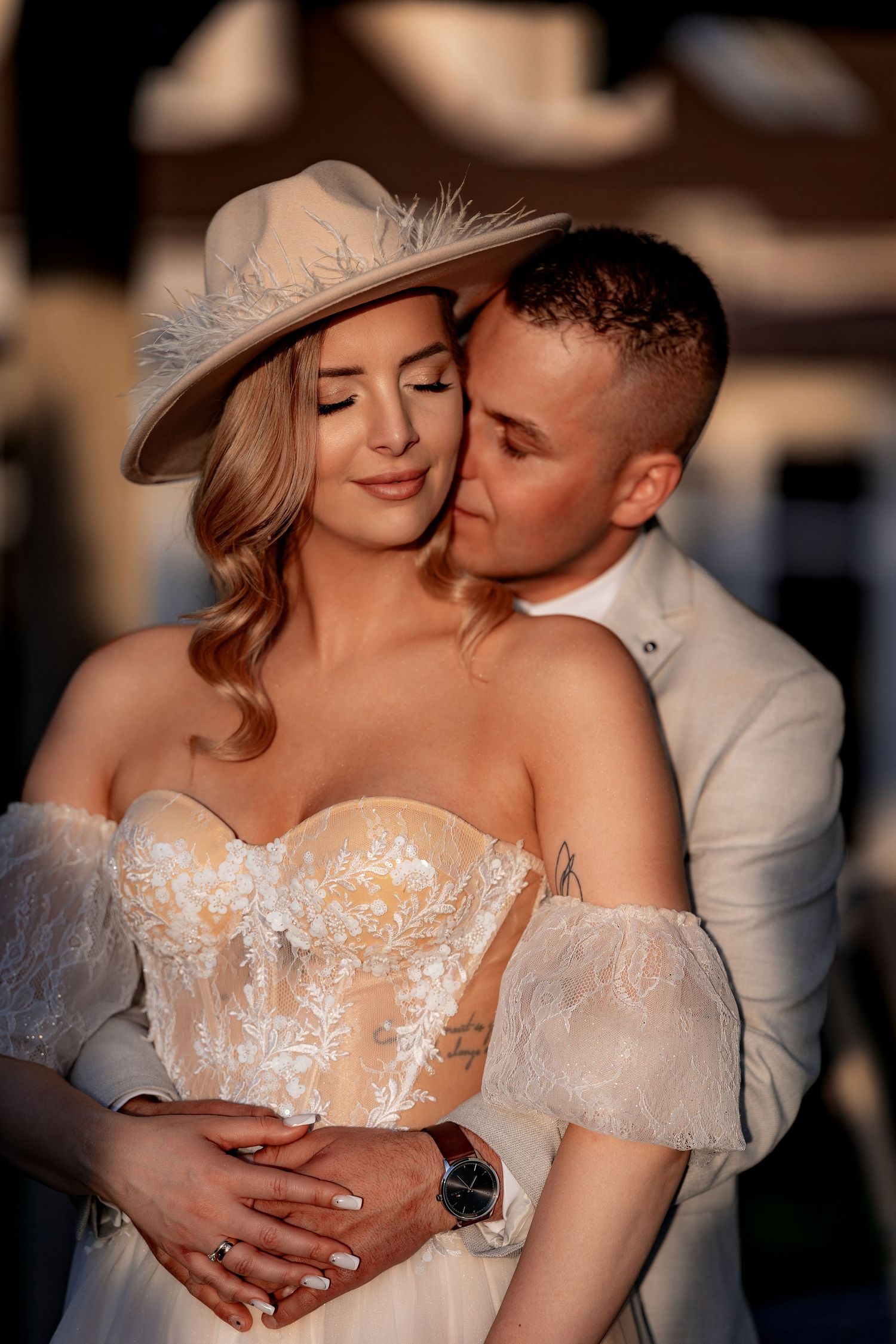 Romantic sunset portrait of couple embracing, bride in lace dress and beige hat.