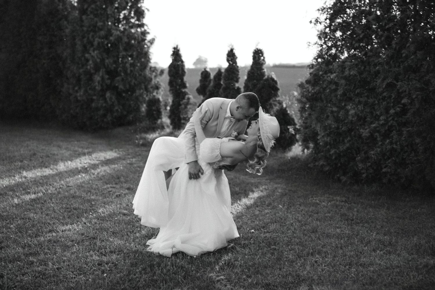 Romantic black and white photo of couple in classic wedding pose on garden path.