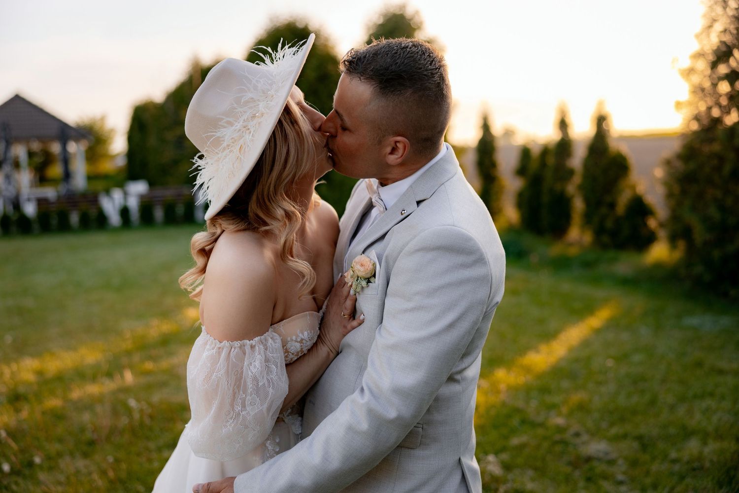 A romantic sunset moment outdoors with a couple in wedding attire sharing a tender kiss.