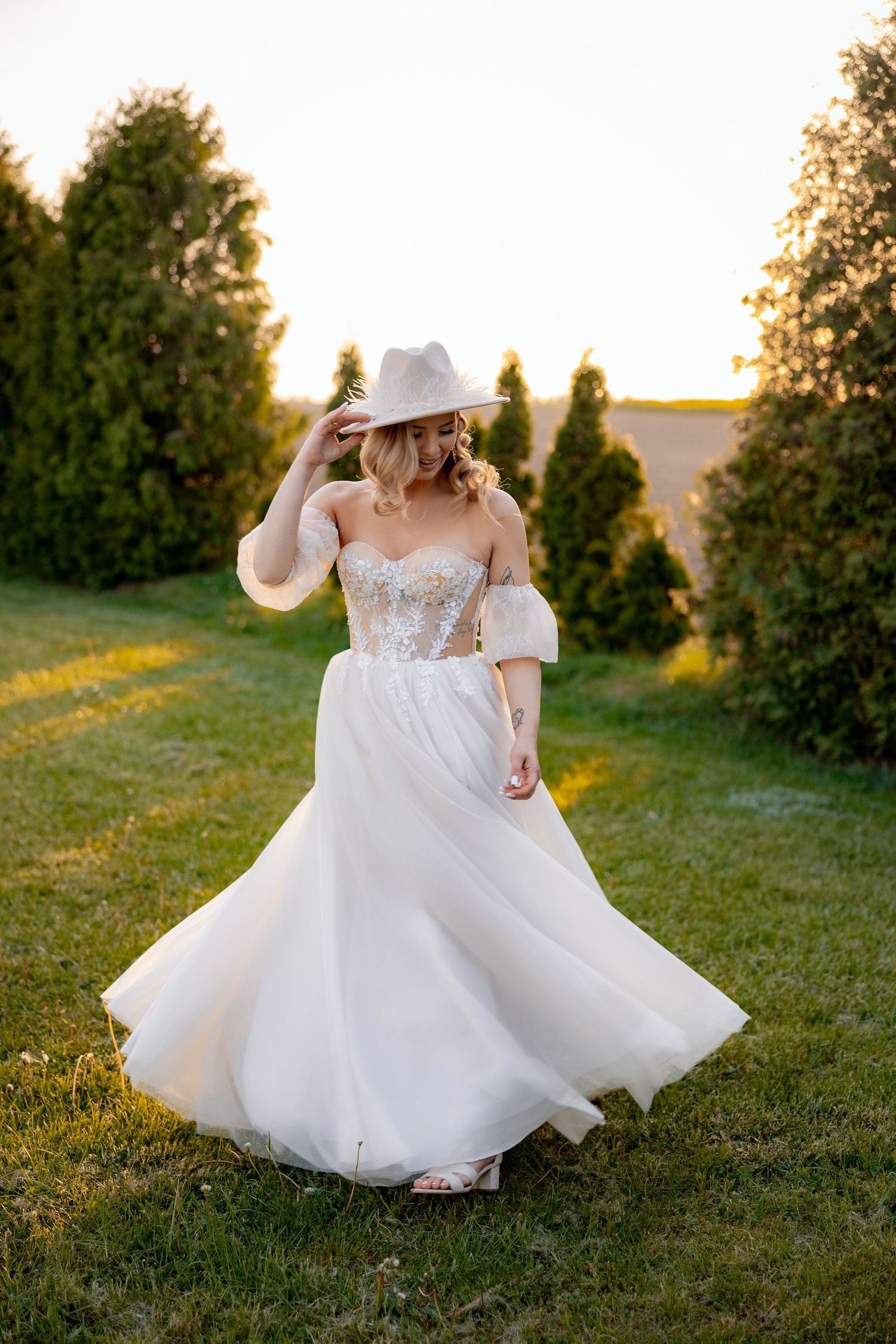 A flowing white wedding gown twirls in golden sunlight against a backdrop of evergreen trees.
