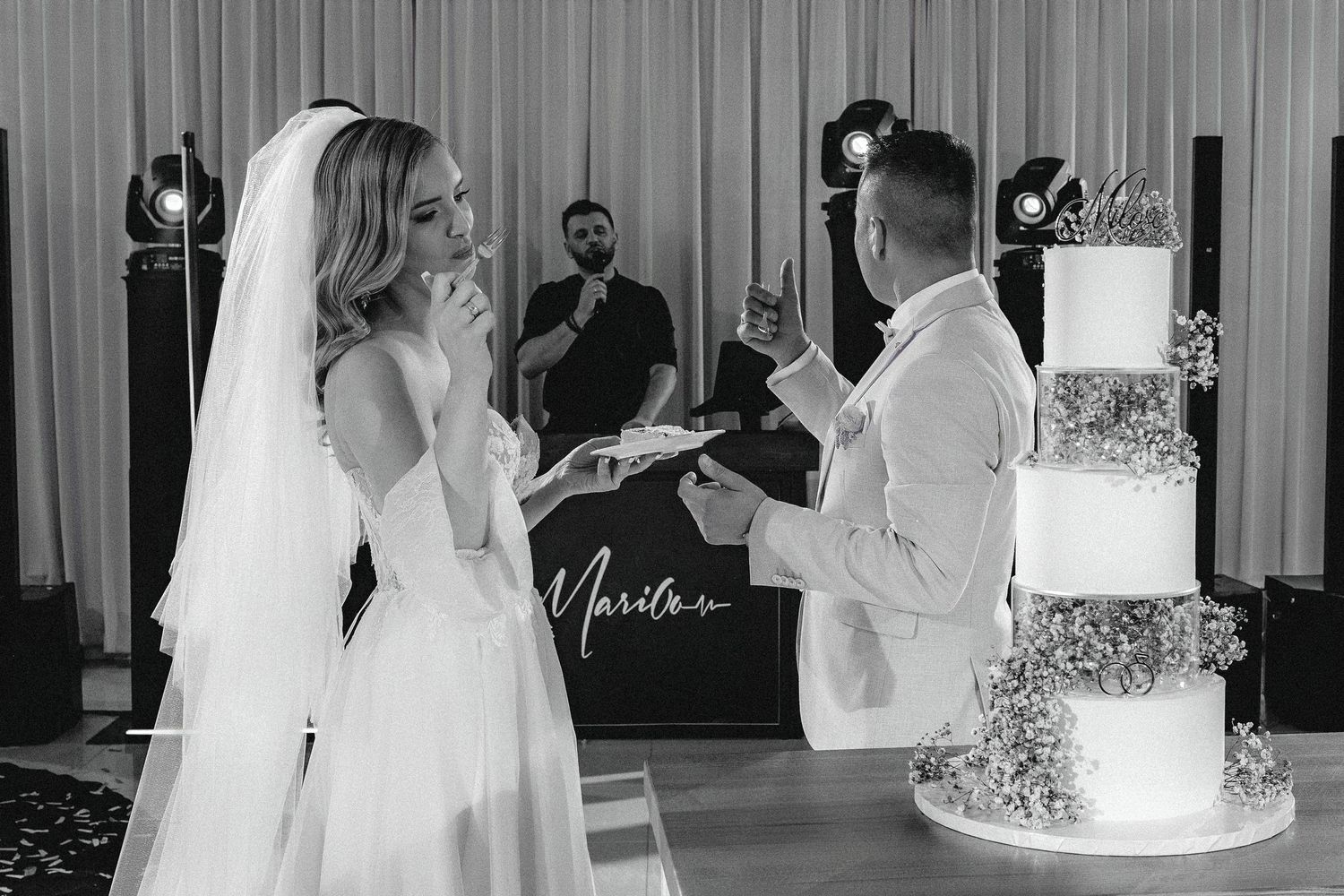 Couple stands before their elegant white wedding cake during their reception celebration.