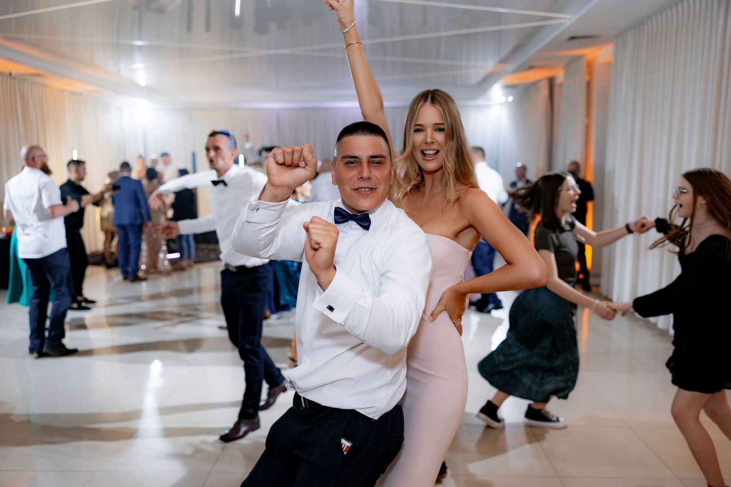 Wedding guests dancing and celebrating on illuminated dance floor at reception.