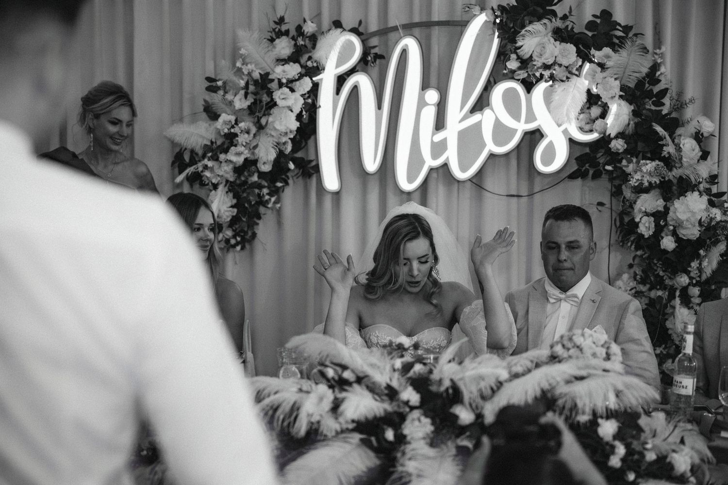 Wedding celebration setup with neon sign and floral arch decorations.