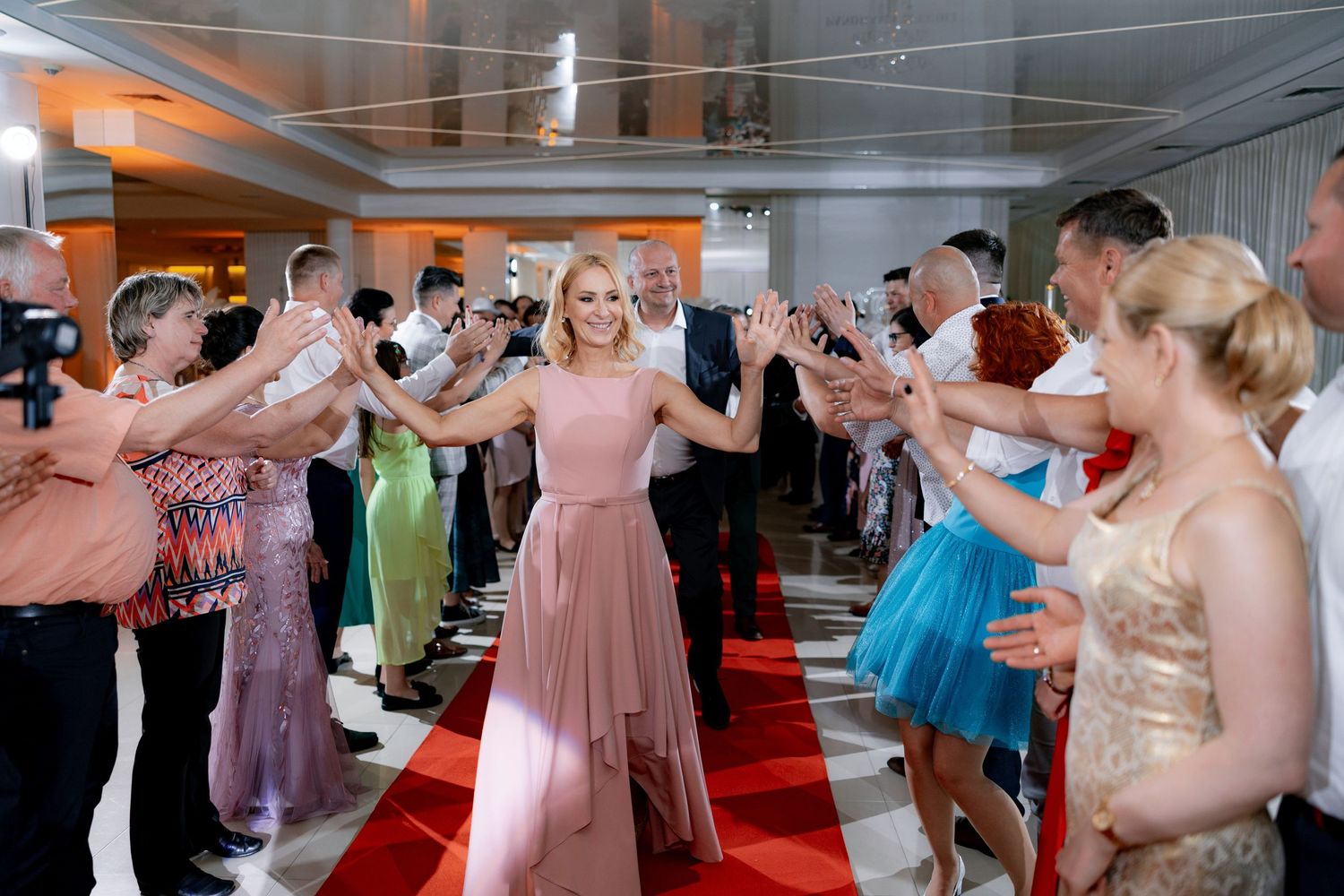 Wedding guests in colorful attire forming a reception line on red carpet.