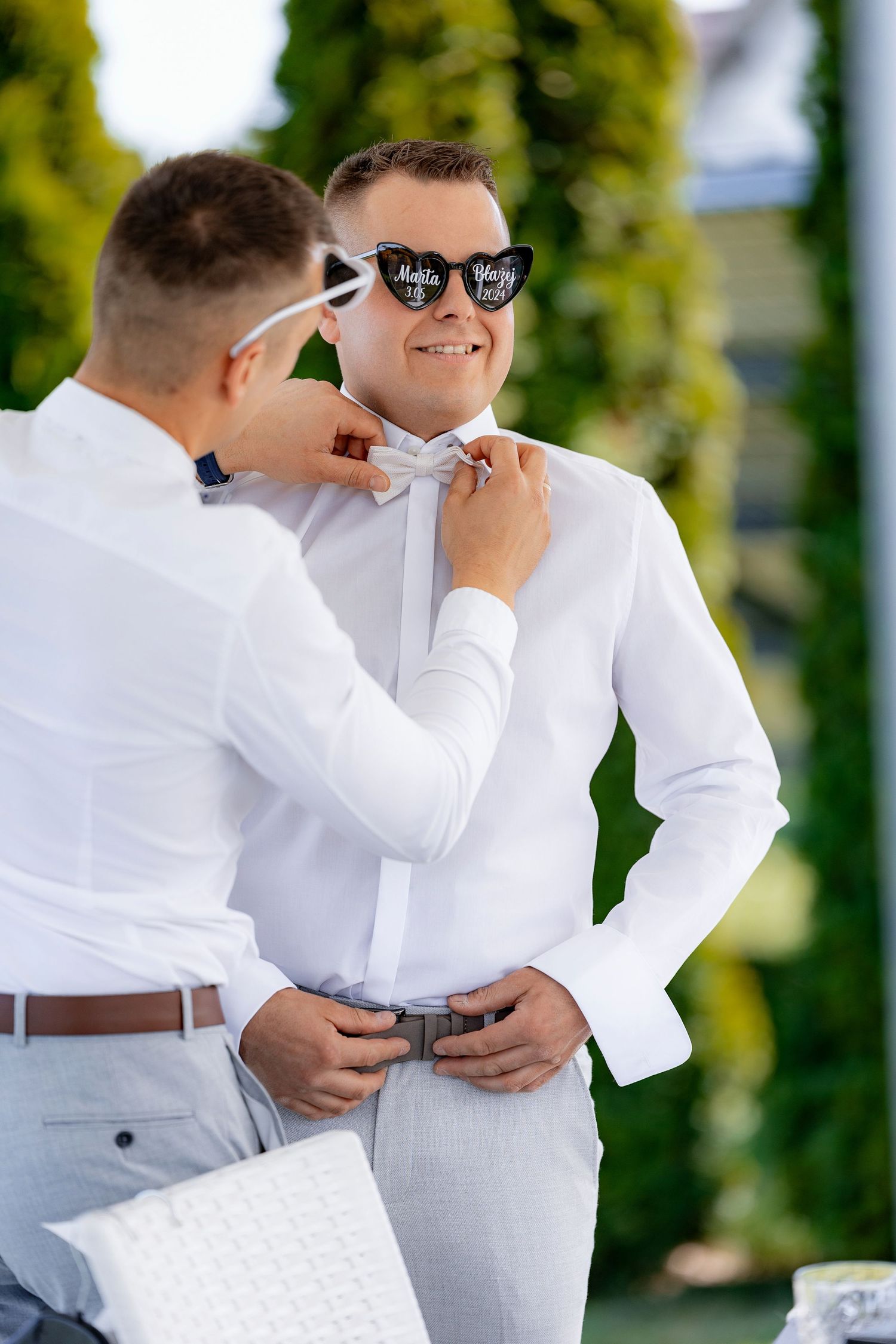 Wedding preparation scene with formal attire adjustments outdoors.