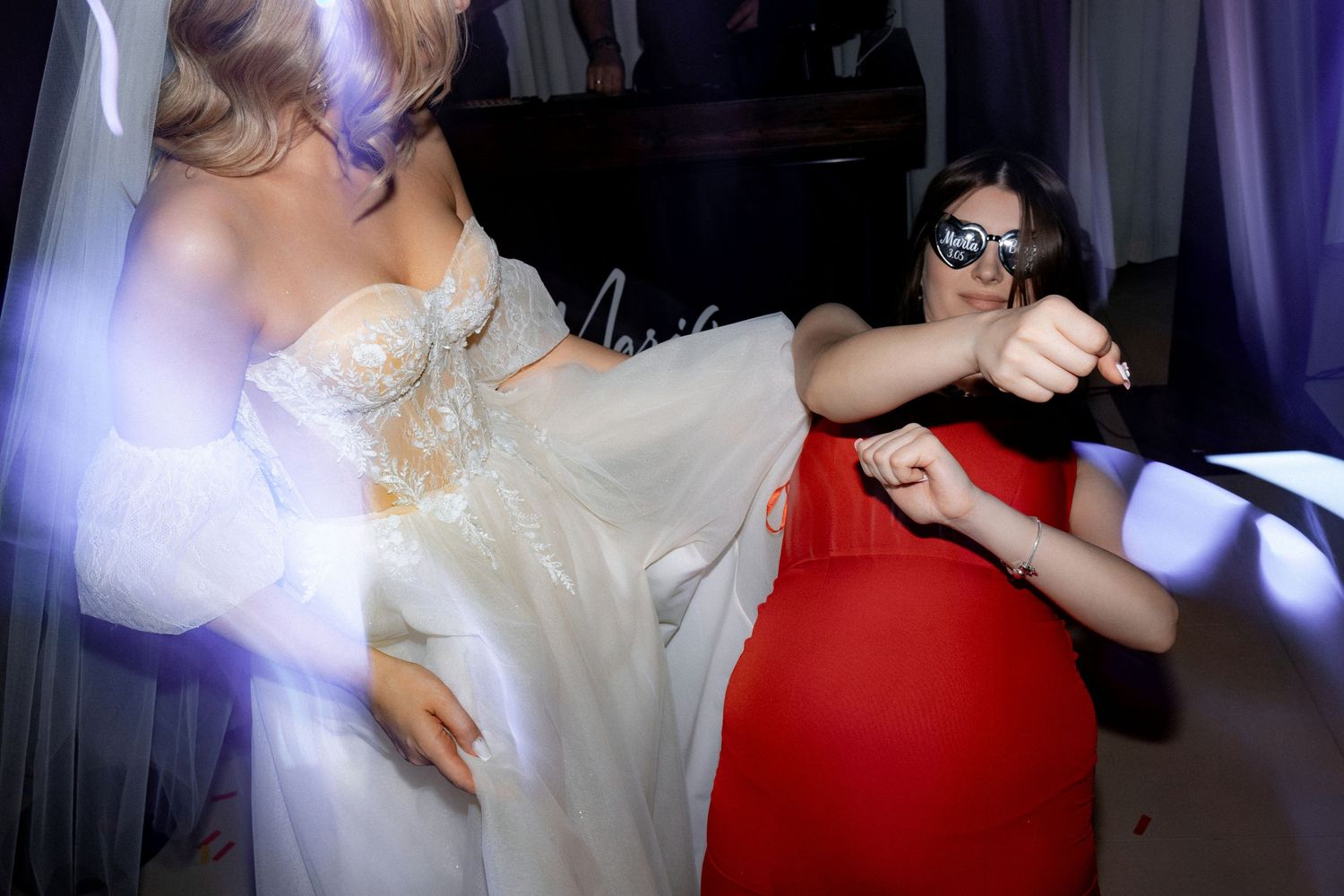 Bride in white dress and guest in red dancing energetically at a wedding reception.
