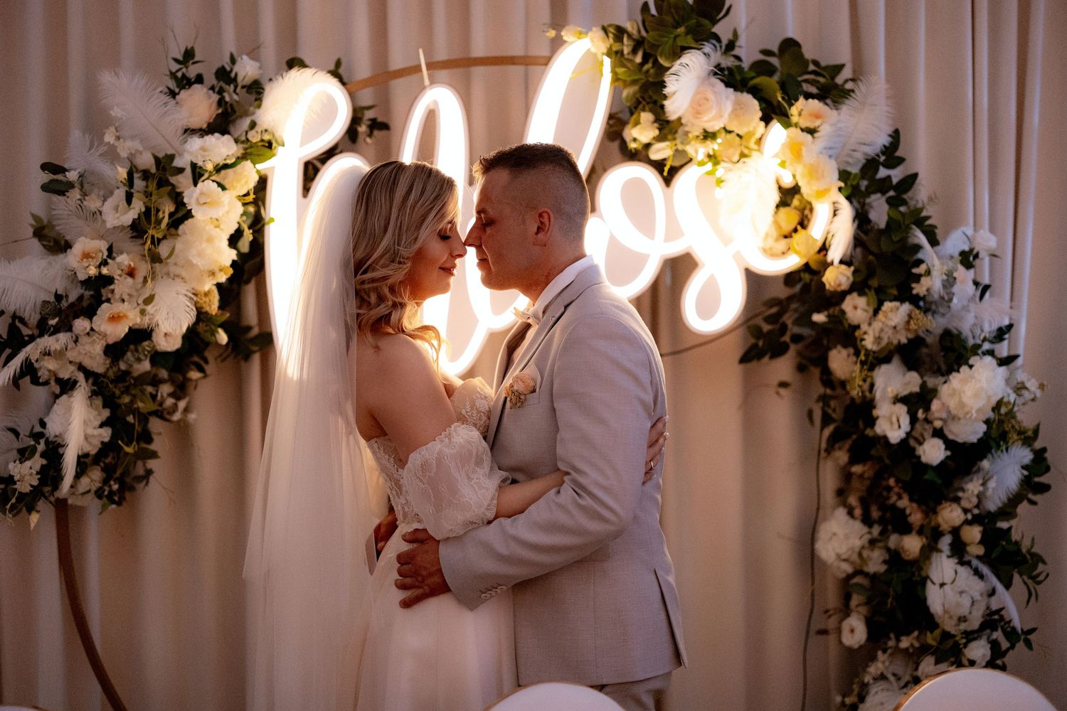 Romantic wedding ceremony with neon sign and floral arch backdrop.