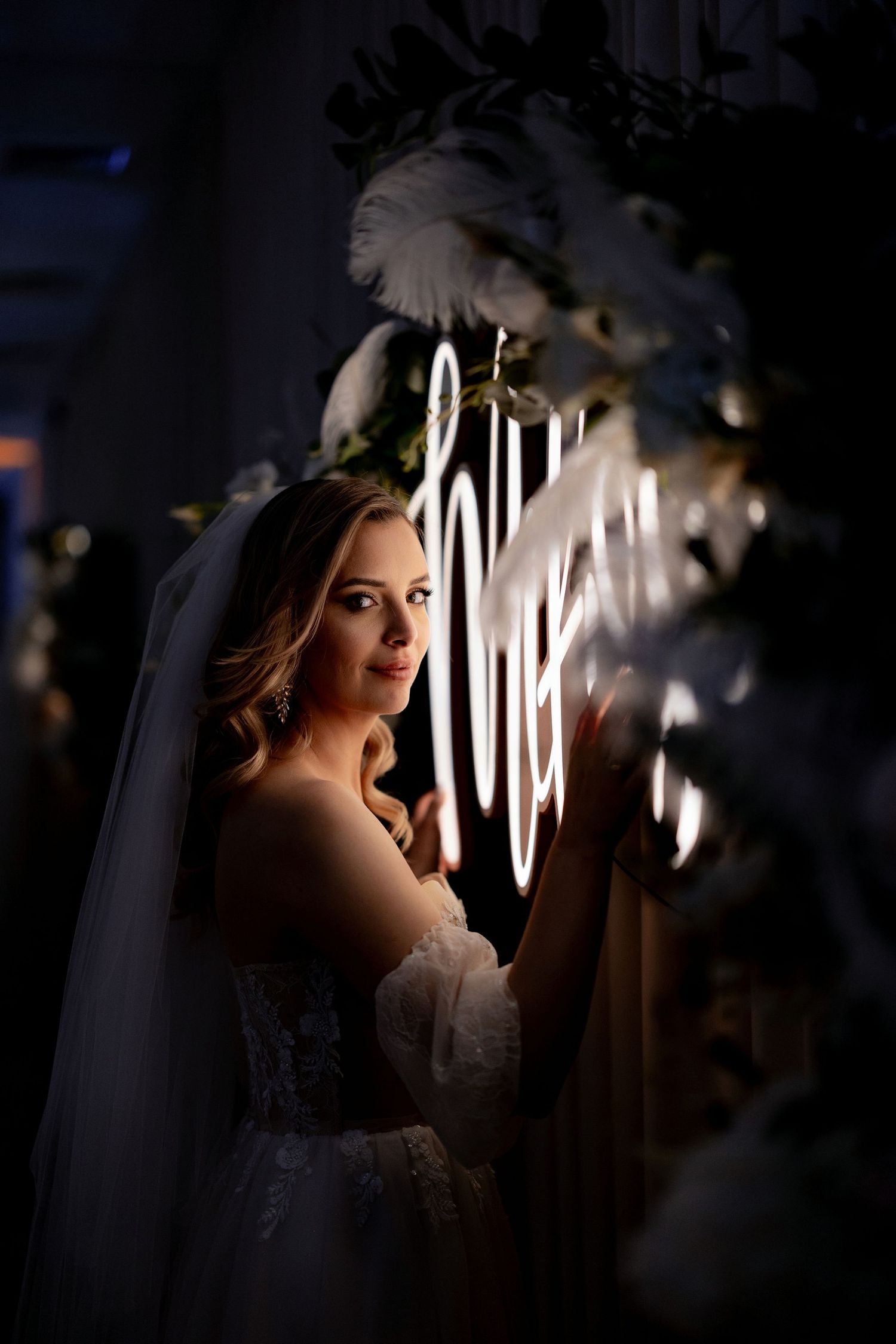 Dramatic side-lit bridal portrait with neon lighting and white floral decorations.