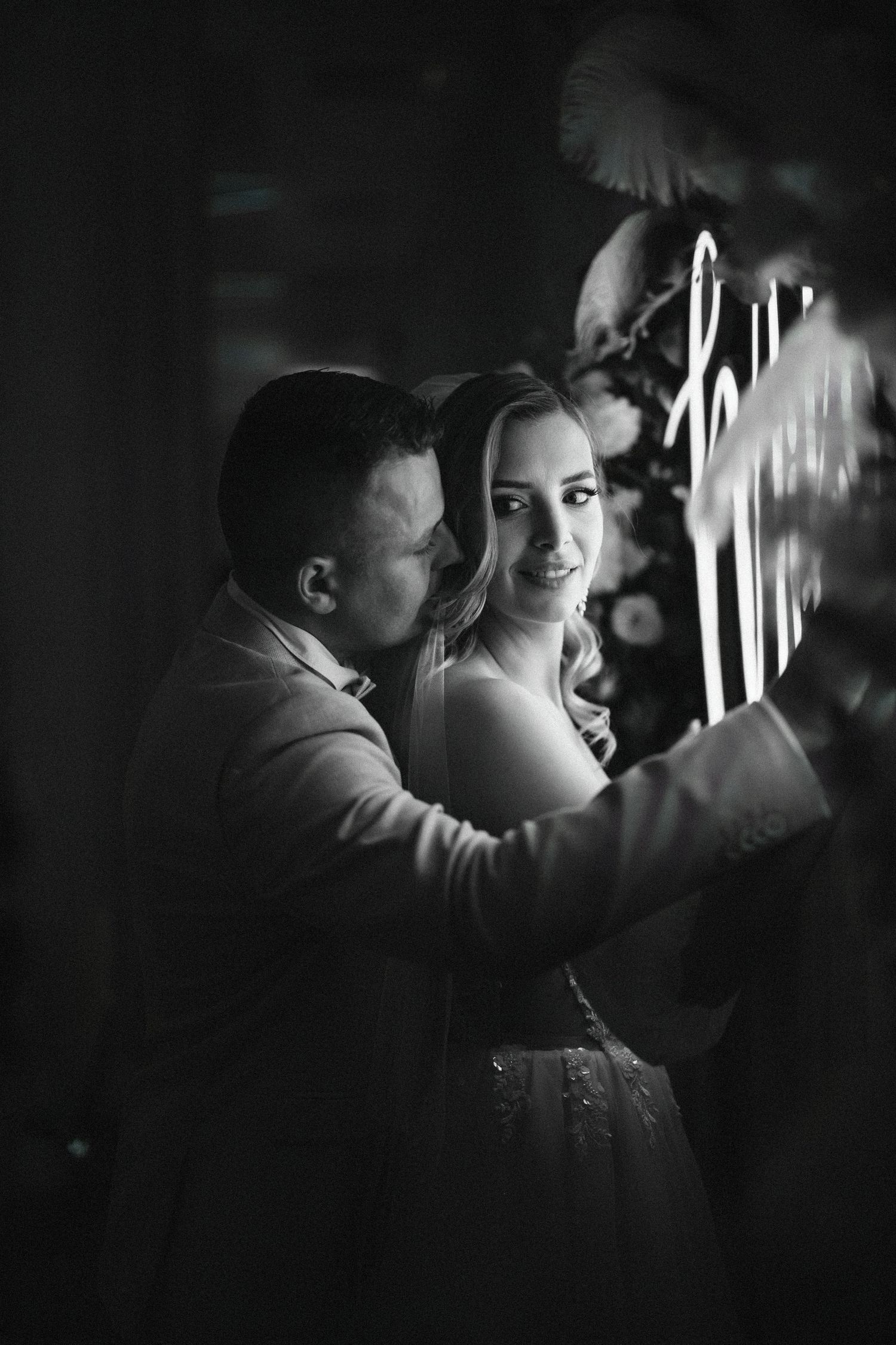Artistic black and white wedding photo with couple illuminated by neon lighting.
