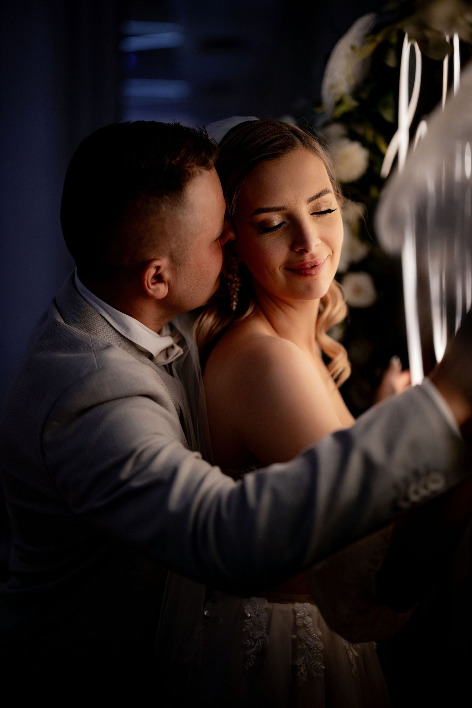 Intimate wedding portrait with moody lighting and neon sign backdrop.