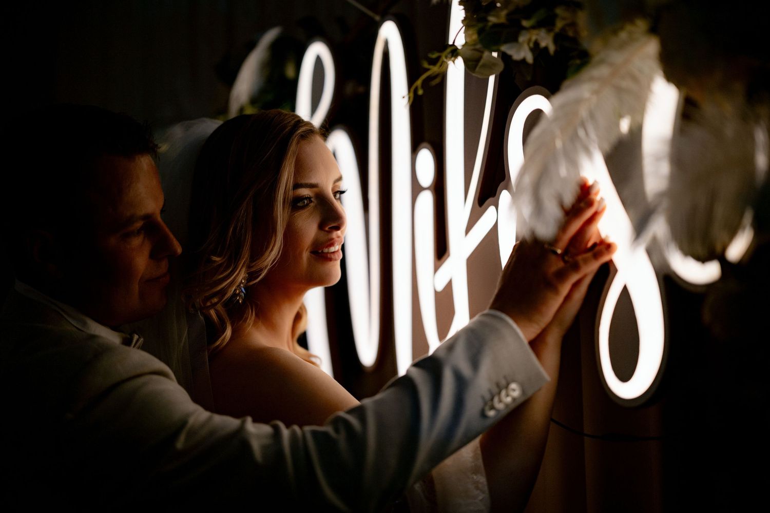 Atmospheric wedding photo with couple silhouetted against illuminated neon signage.