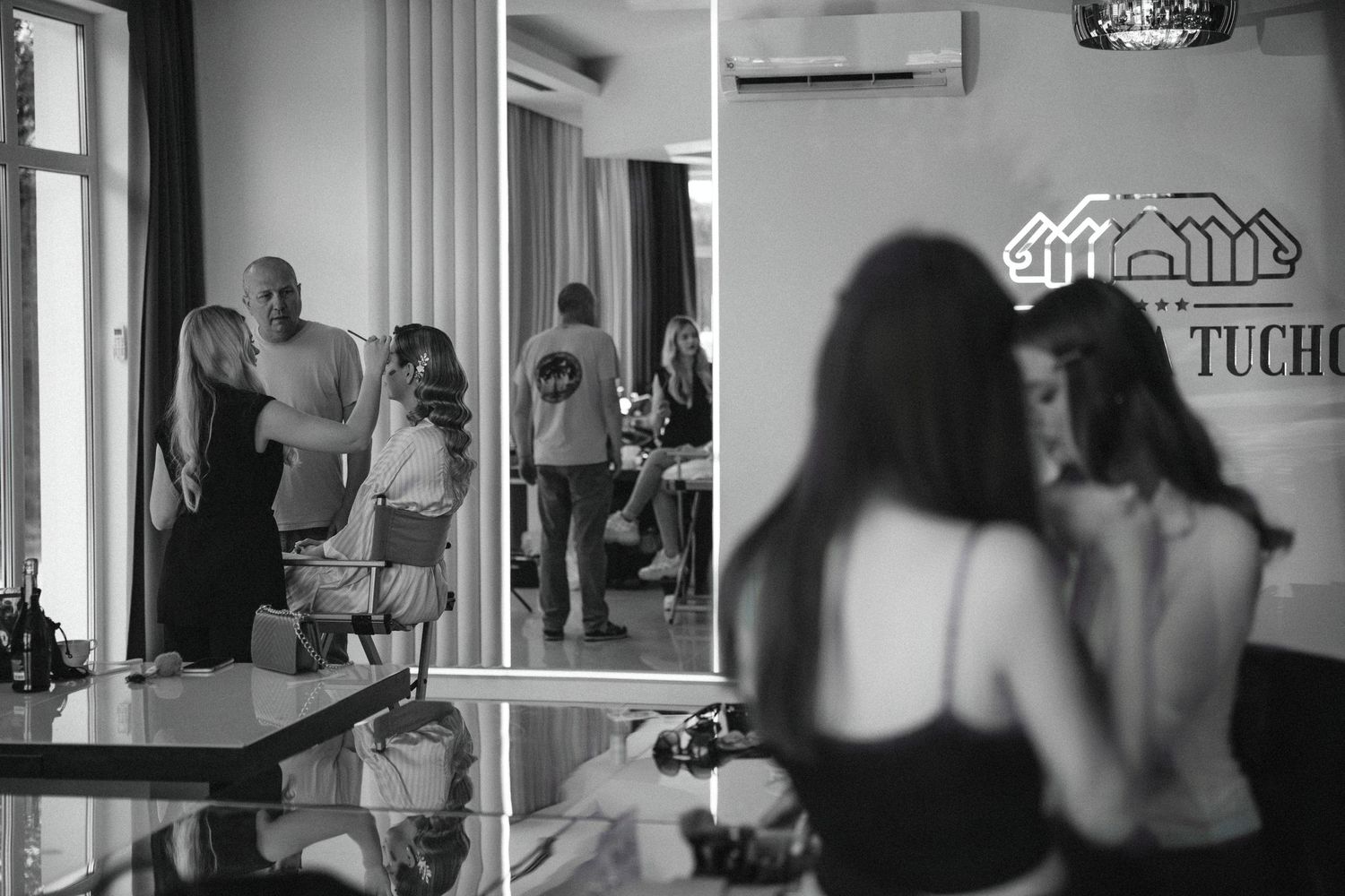 A black and white photo showing wedding preparation activities in a bright indoor space.