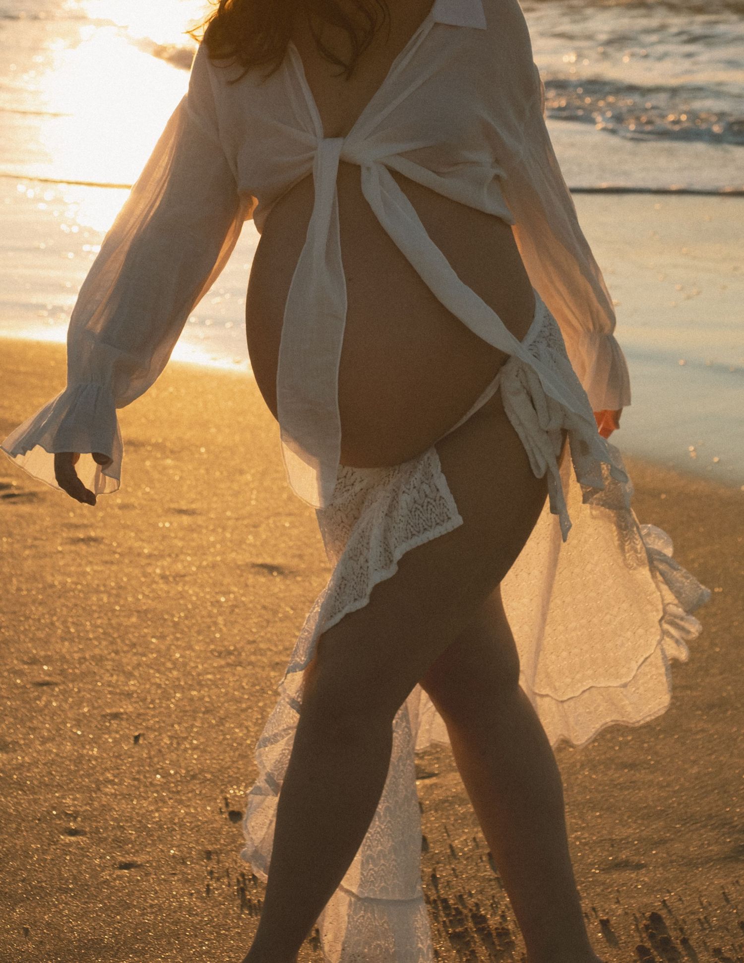 Woman in white beach cover up walking on sandy shore during golden hour.