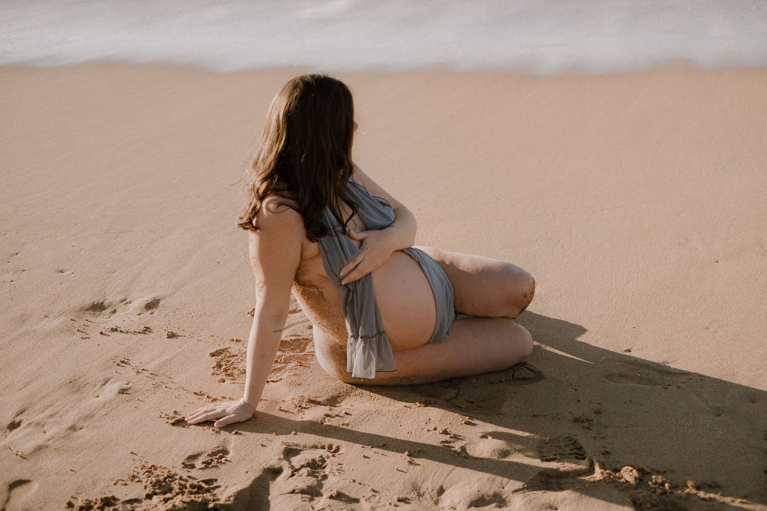 Figure in casual attire reclining on beach sand during golden hour.