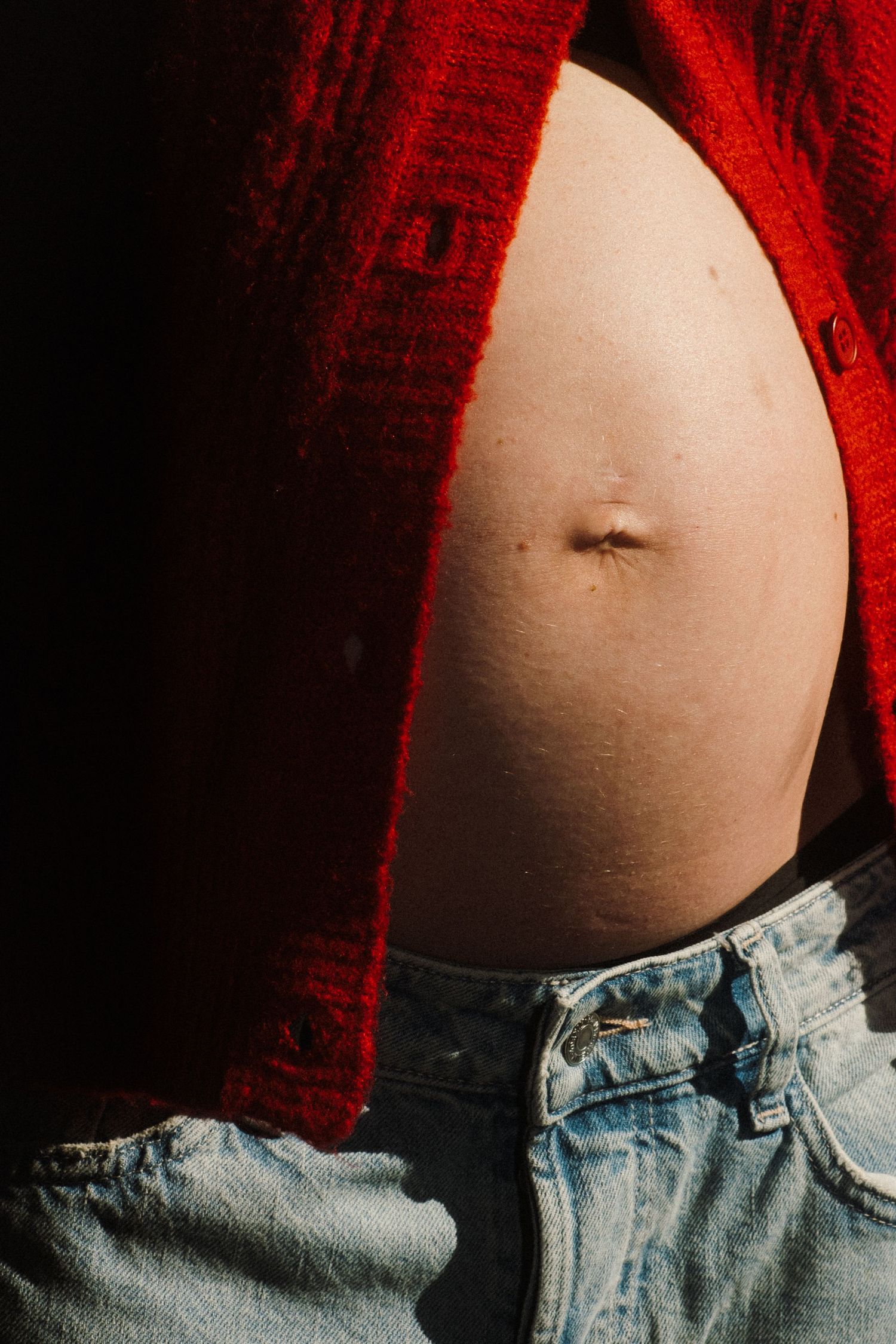 Close-up of a pregnant belly with a red sweater and blue jeans.