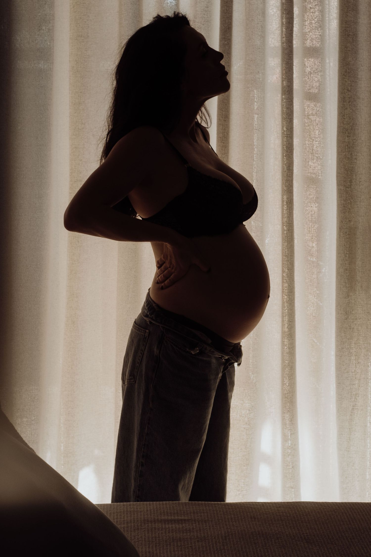 Dramatic backlit silhouette of an expectant mother against white curtains.