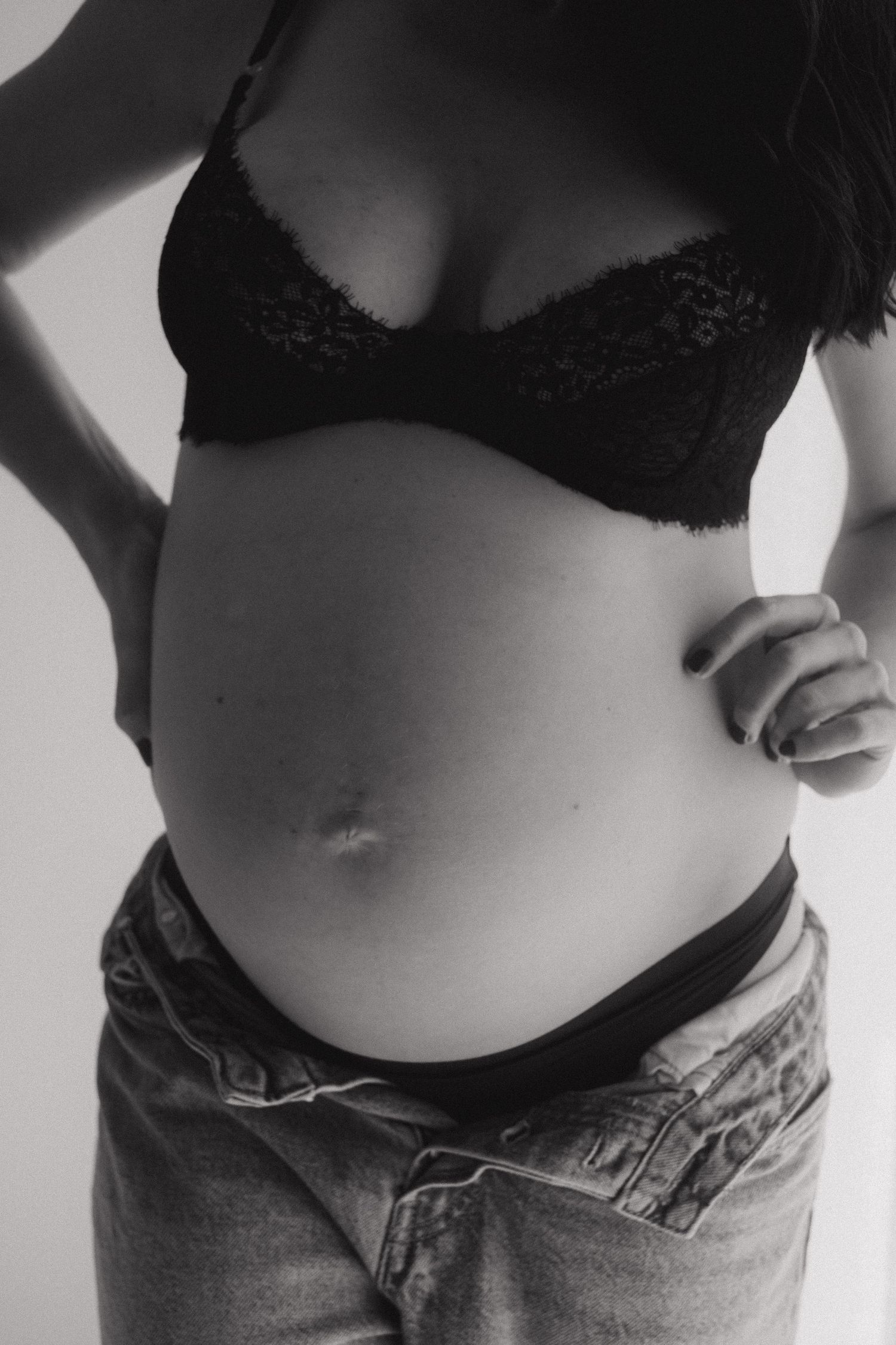 Black and white close-up of a pregnant belly with black lace bra and denim.