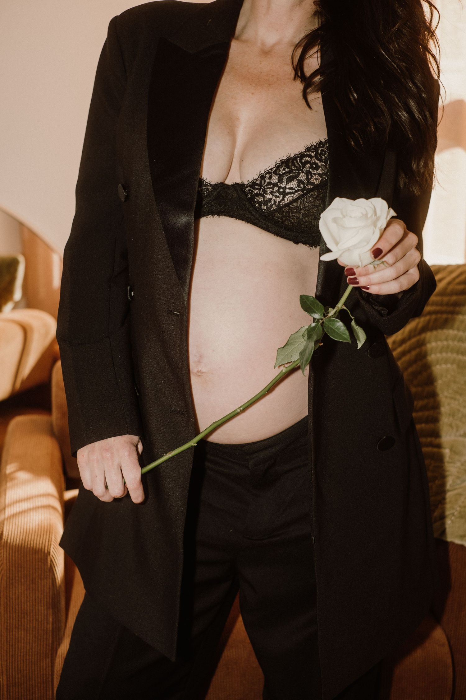 An artistic maternity portrait with a white rose against black attire in warm lighting.