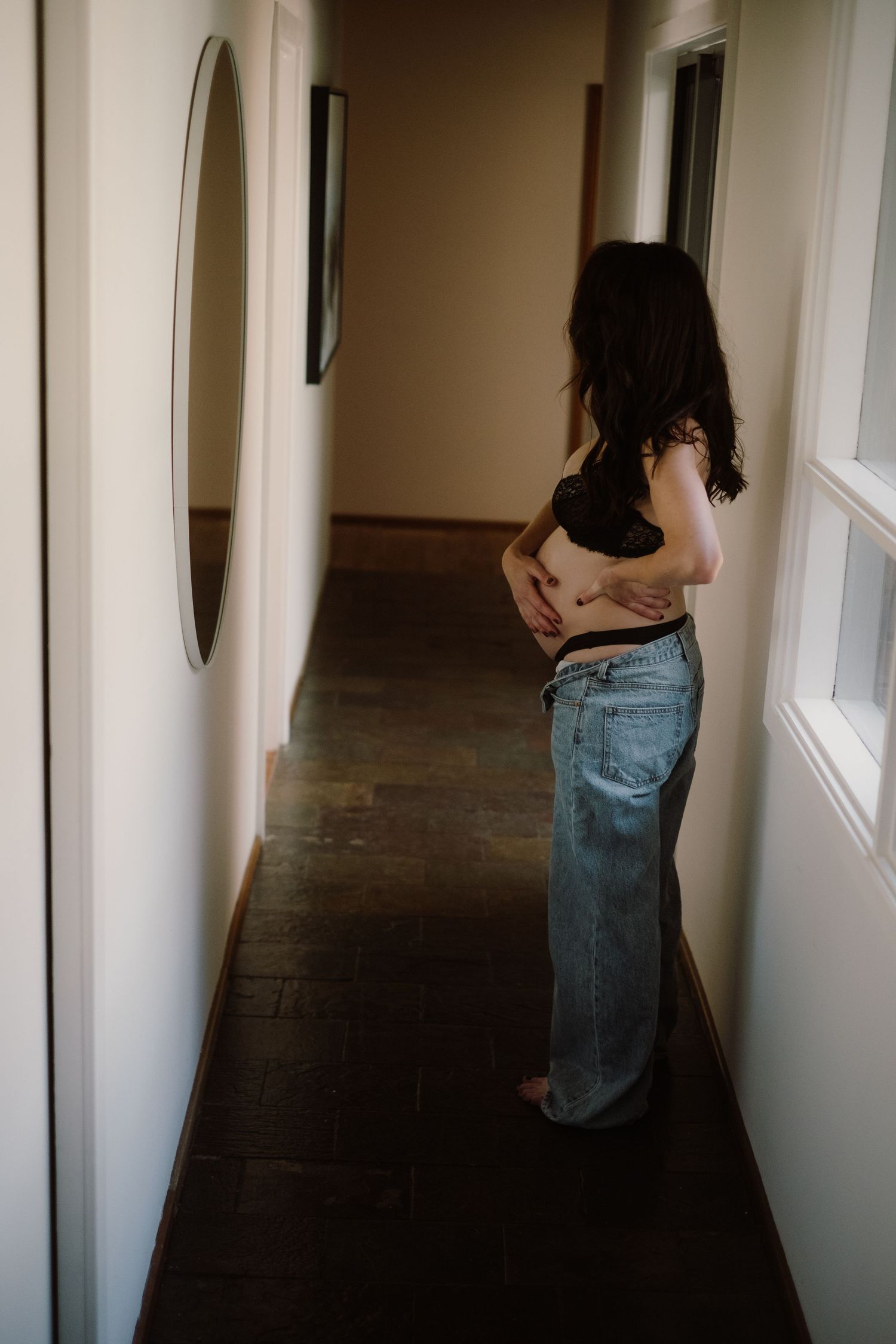 A dark hallway scene with a round mirror and wooden floors showing a casual outfit with baggy jeans.