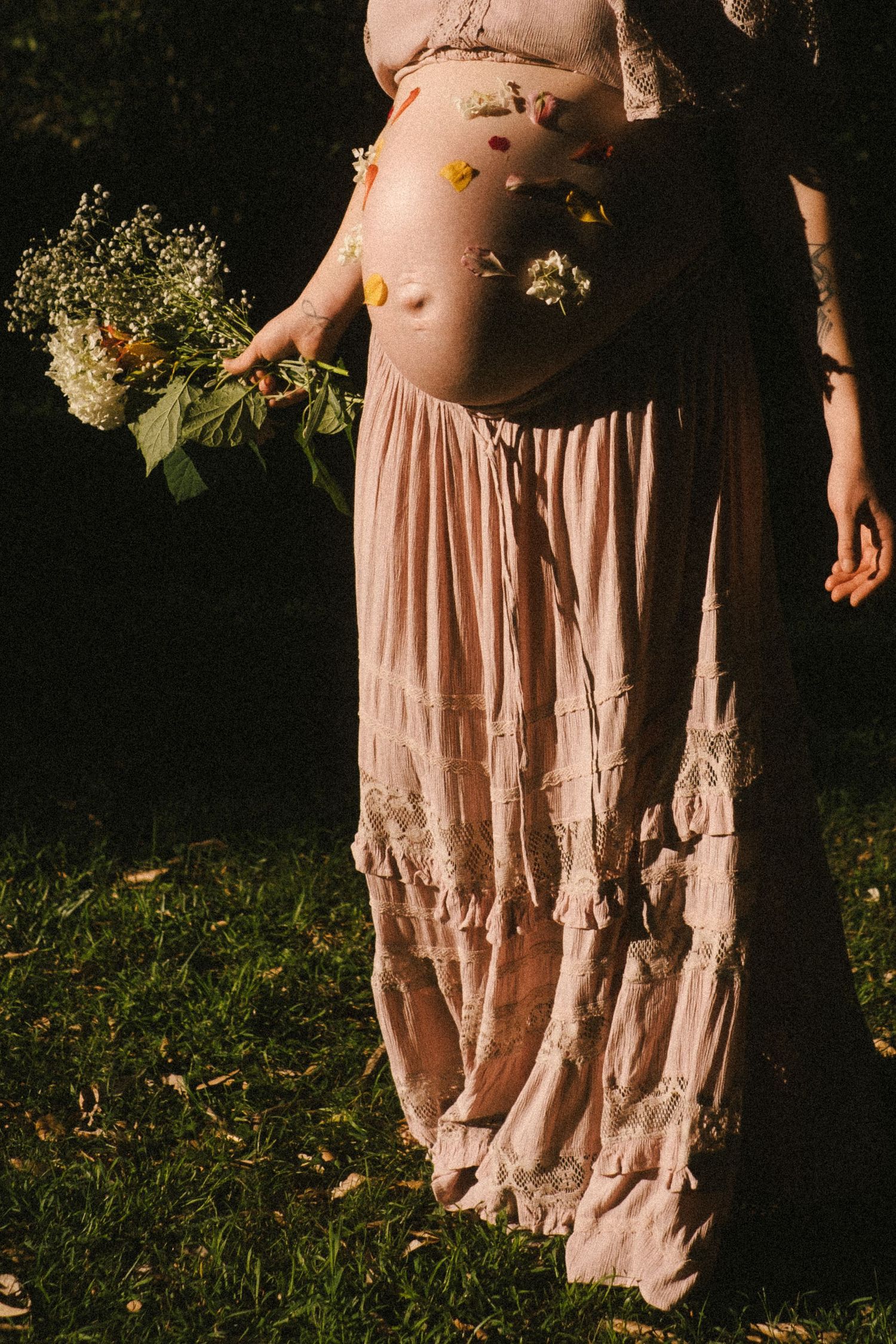 Close-up view of a flowing blush pink ruffled dress skirt photographed in warm sunlight against grass and fallen leaves.