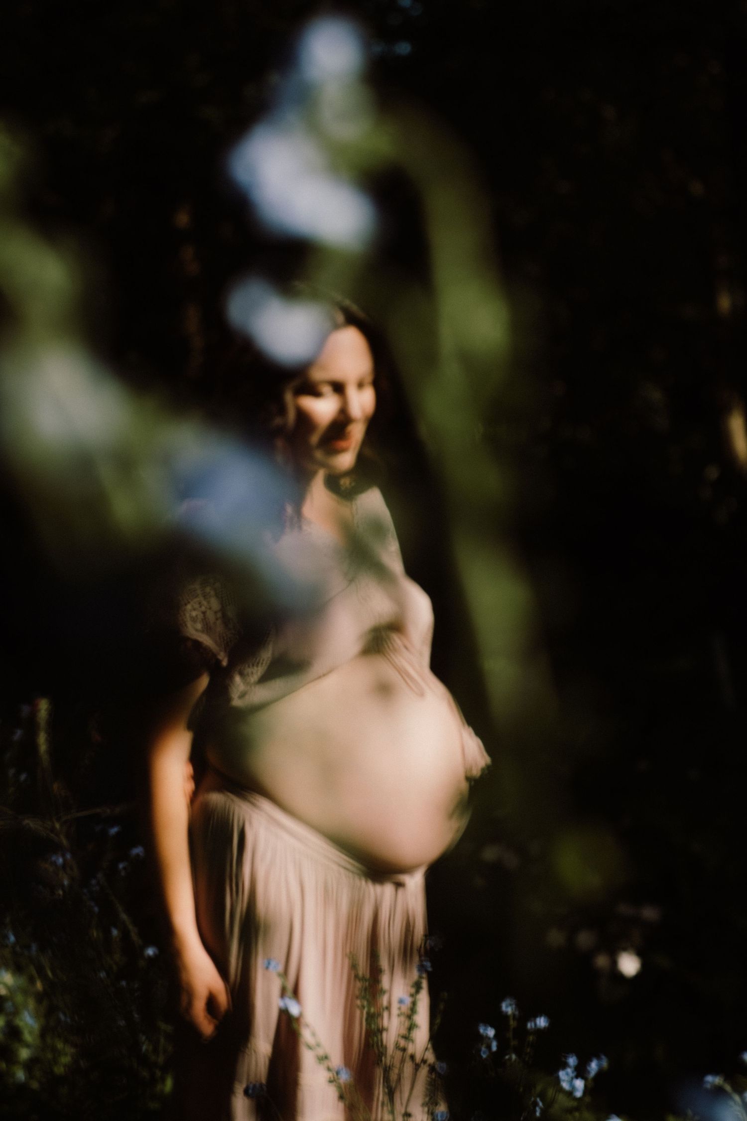A dreamy maternity photo session in a forest setting with soft natural lighting and bokeh effects.