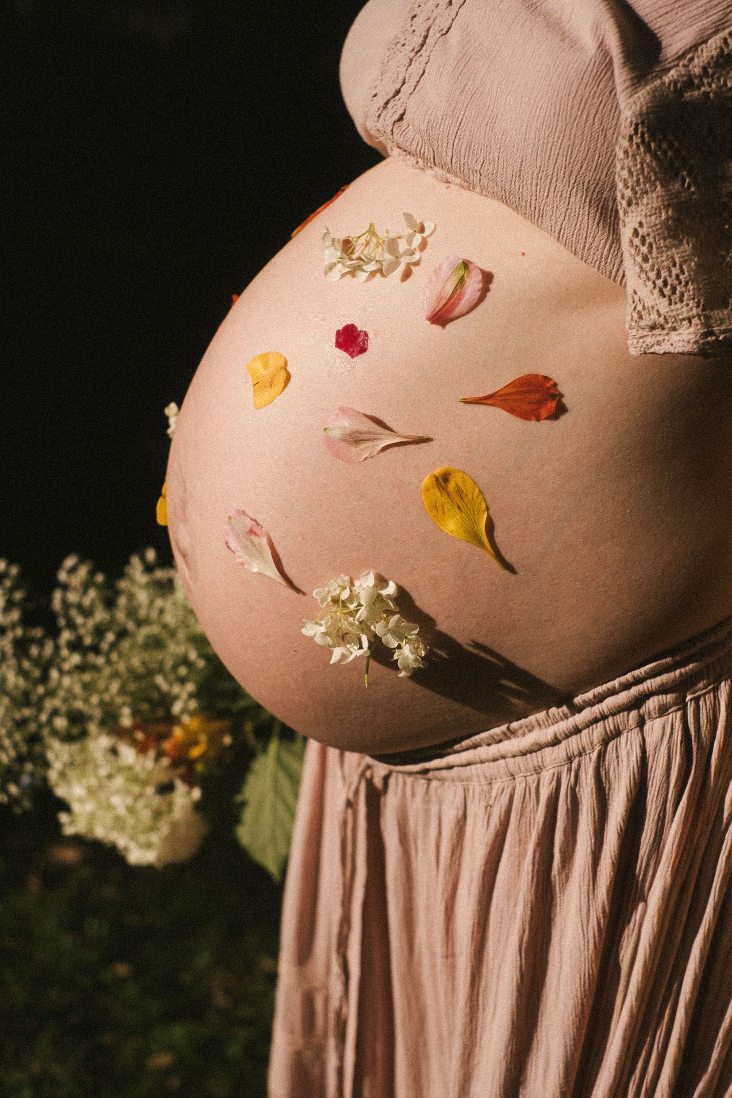 A sequence of artistic photos showing a pregnant belly adorned with delicate flower petals in warm lighting.