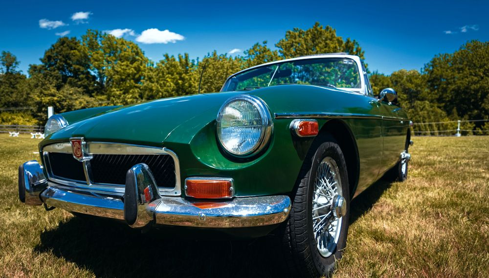 British racing green Jaguar E-Type photographed against trees and cloudy blue sky.