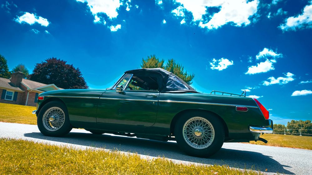 Classic green convertible car photographed from the side against a bright blue sky with white clouds.