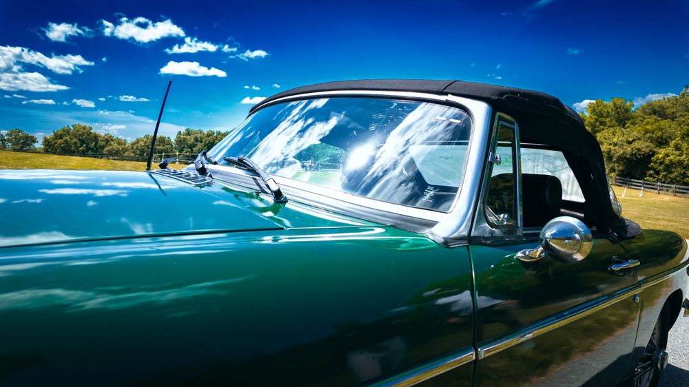 Vintage green convertible car with black soft top shown in close-up profile view.