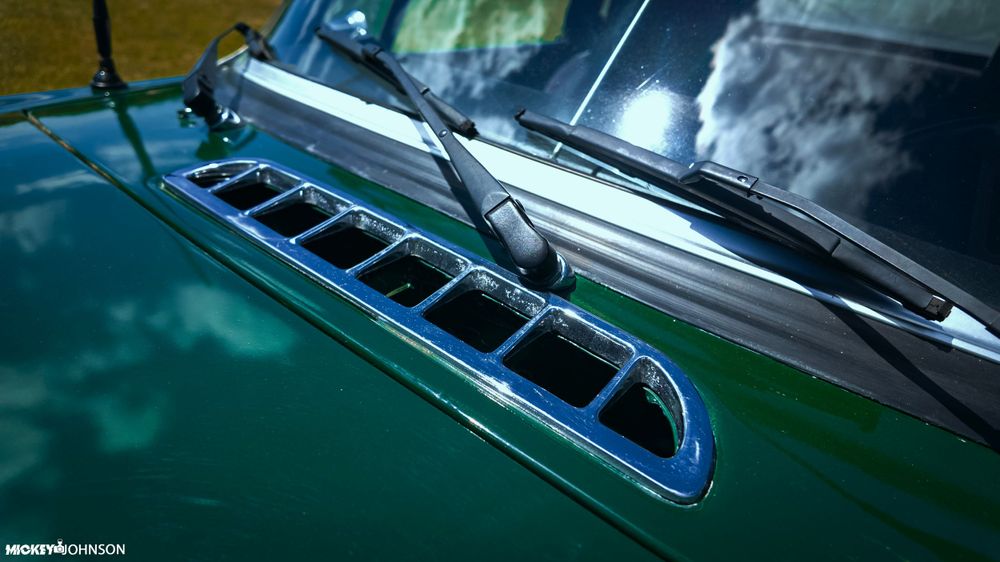 Chrome hood scoop detail on a classic green car with water droplets.