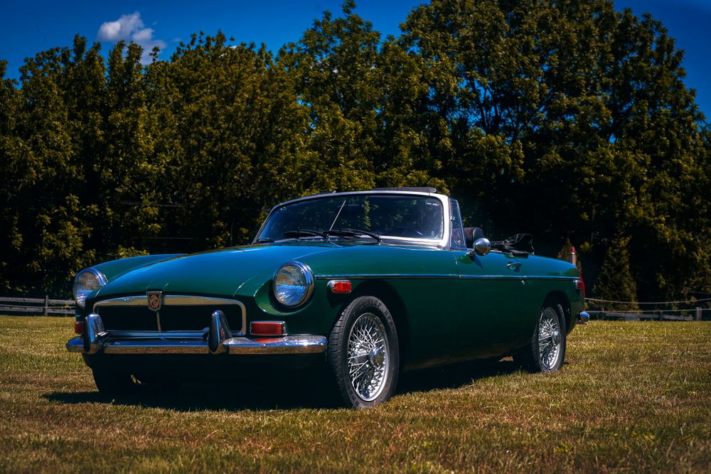 Classic vintage convertible cars lined up in a row against a blue sky and trees.