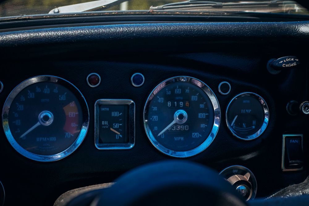 Detailed view of classic car instrument panel with multiple gauges in low light.