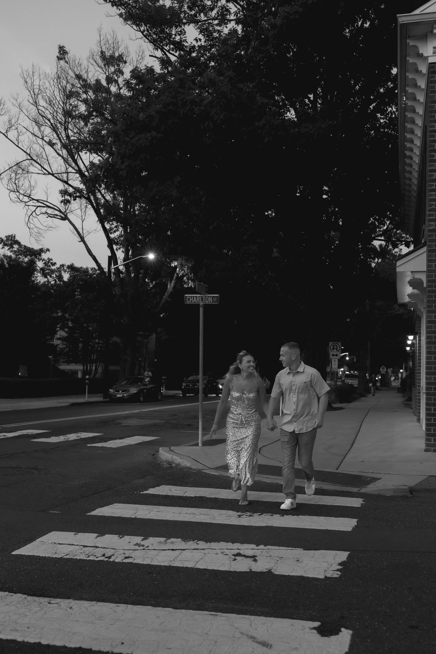 Black and white nighttime street scene with pedestrians walking on crosswalk.
