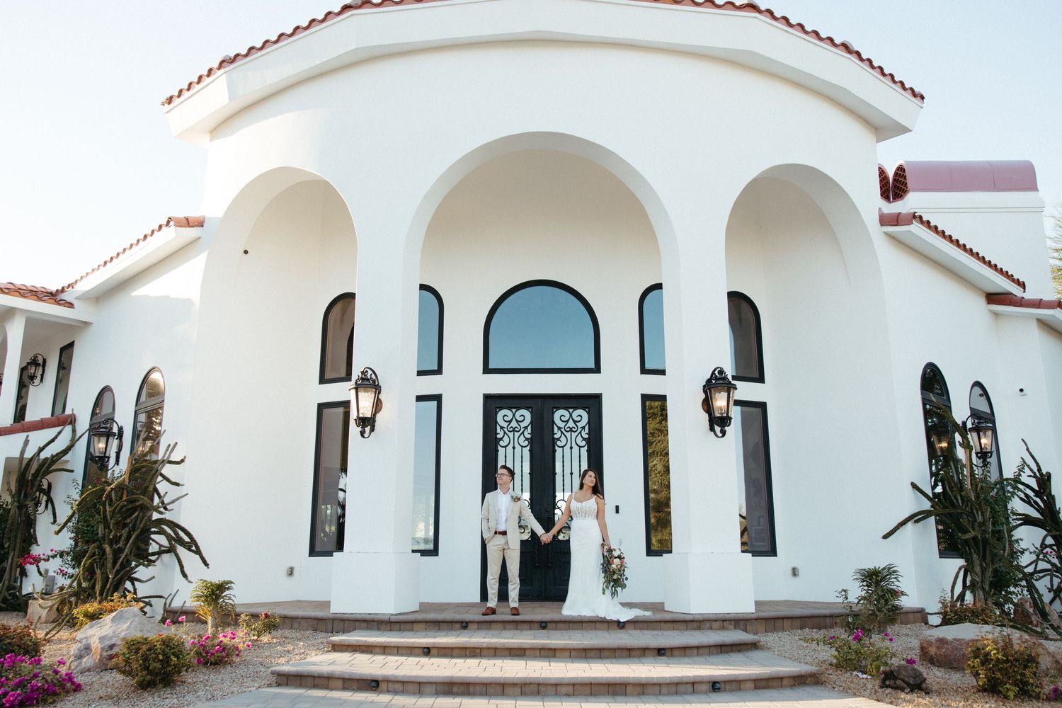 Wedding couple standing in front of a stunning white Mediterranean-style villa with arched doorways.