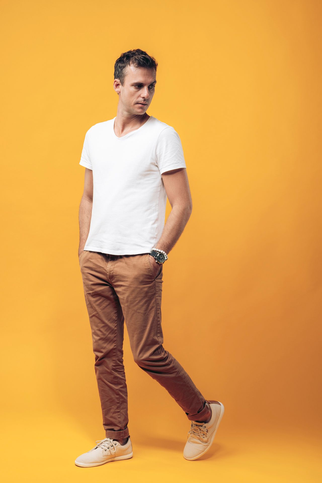 Full length portrait of someone in casual wear posing against an orange background.