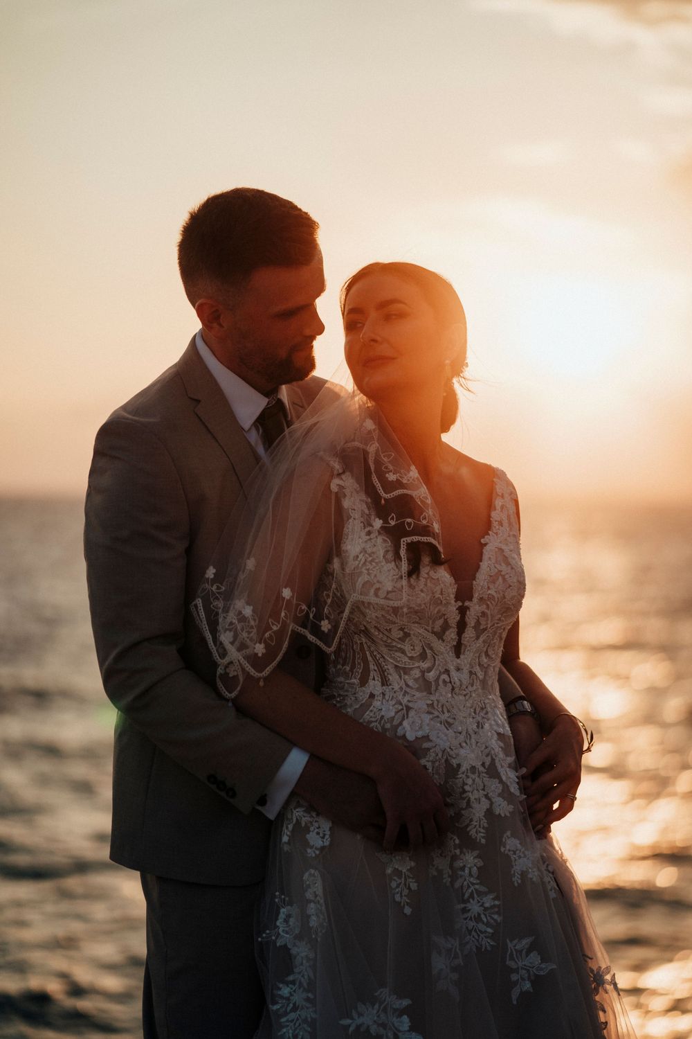 A romantic sunset wedding photo shows a couple embracing by the ocean with golden light glowing on the water.