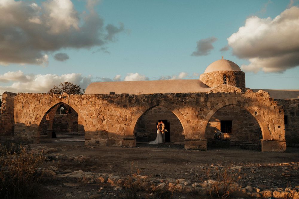 Ancient stone ruins with domed structure and arched passages in warm sunset light against cloudy sky.