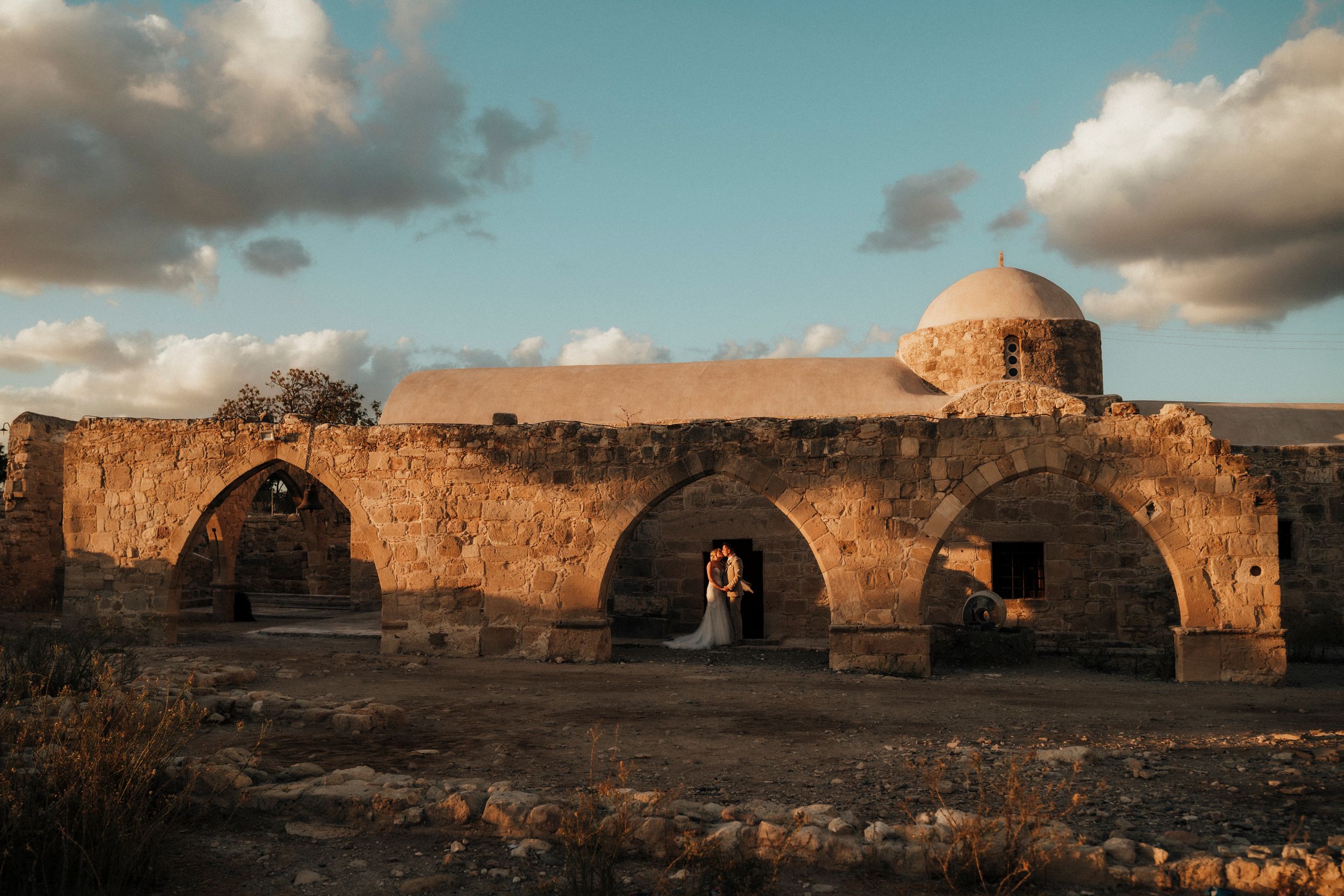 Ancient stone ruins with domed structure and arched passages in warm sunset light against cloudy sky.