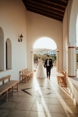 A series of five photos showing a couple walking through a sunlit white archway corridor with wooden benches.