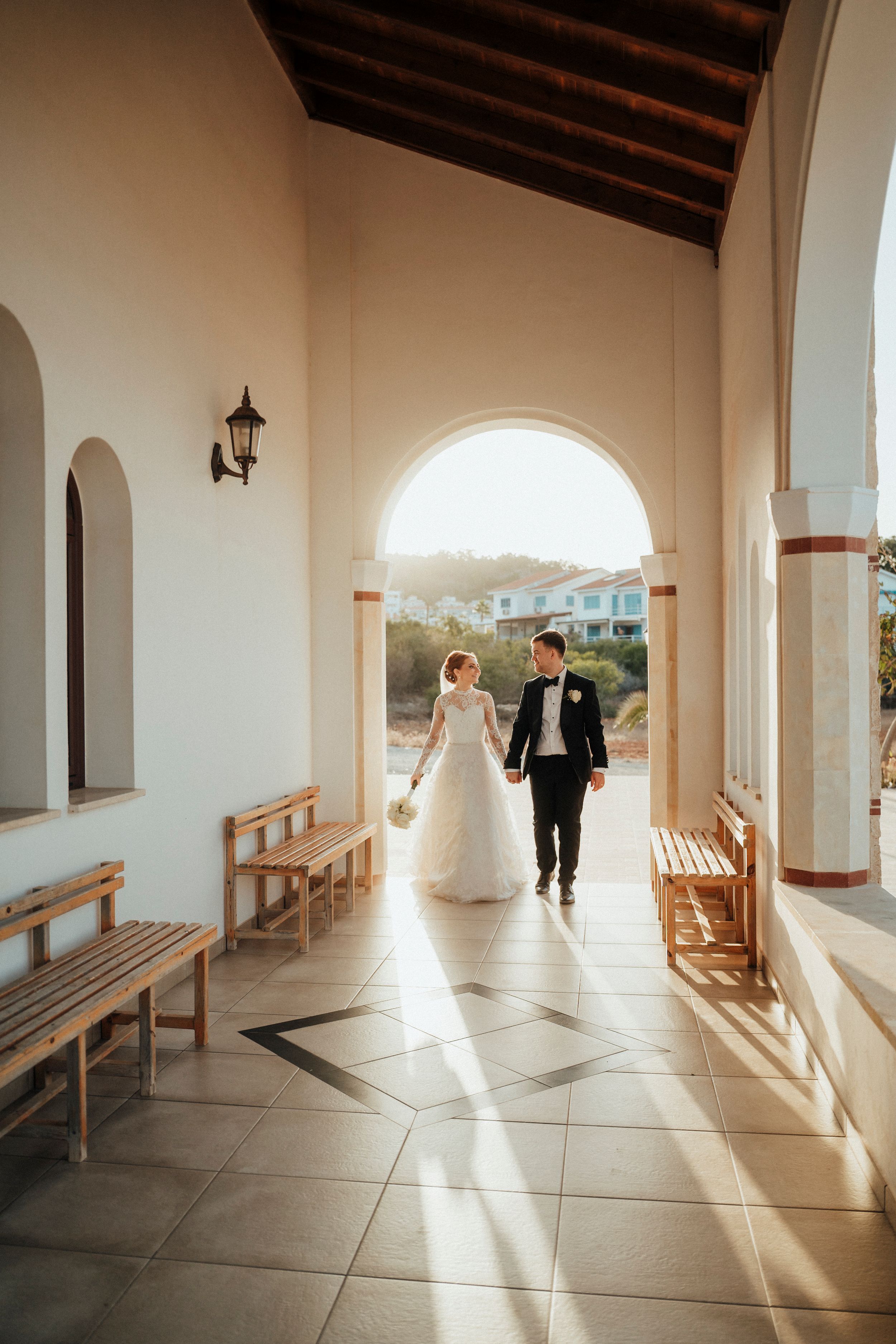 A series of five photos showing a couple walking through a sunlit white archway corridor with wooden benches.