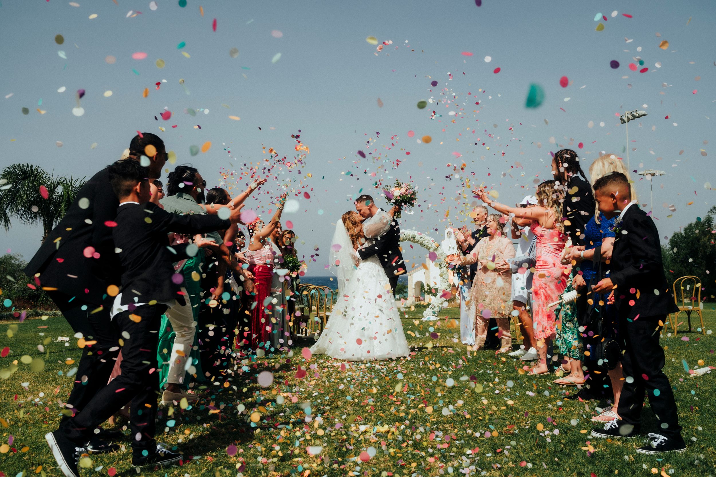 Wedding celebration with colorful confetti being thrown by a joyful group outdoors.