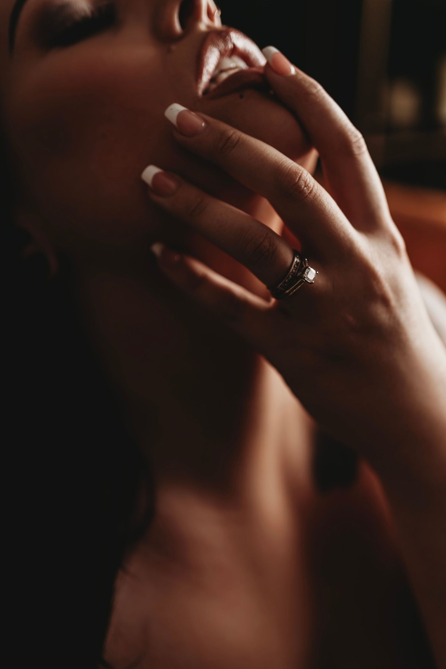 Woman in black lingerie, holding her straps while gazing into the camera, captured in soft, intimate lighting.
