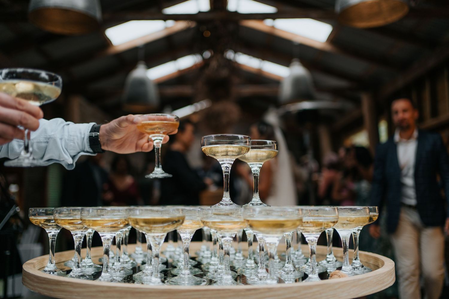 Champagne tower with coupe glasses being served at elegant wedding reception in rustic barn venue.