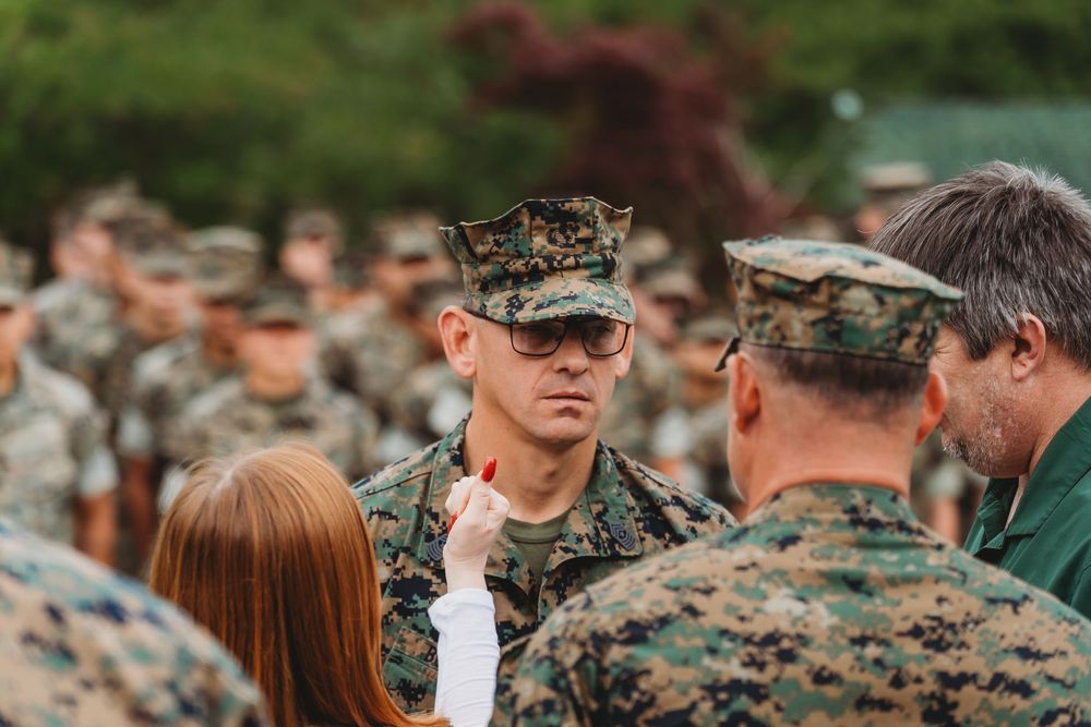 US Marines in camouflage uniforms gather outdoors as an officer speaks with personnel during a military formation.