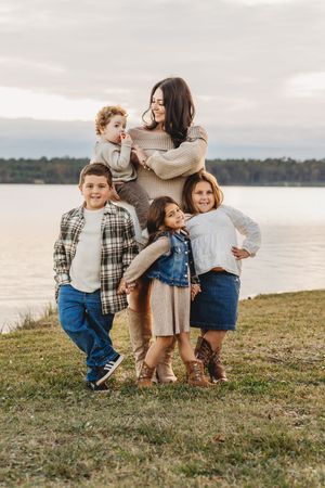 Brunette mother poses with four children near a lake during golden hour outdoors. Jacksonville, NC