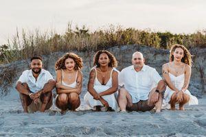 Blended family of five in white outfits sits together smiling on a sandy beach. Jacksonville, NC