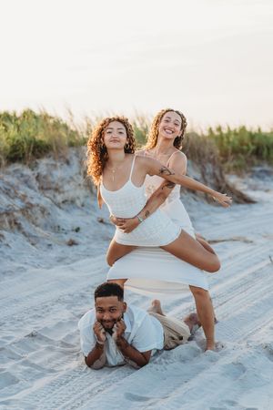 Three young adults in white outfits pose playfully on a sandy beach at sunset. surf city photographer