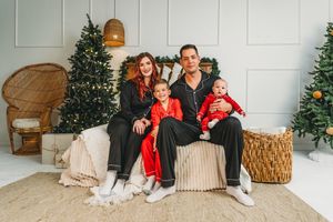 Family of four in matching black and red pajamas poses by Christmas trees indoors. Richlands nc family photographer