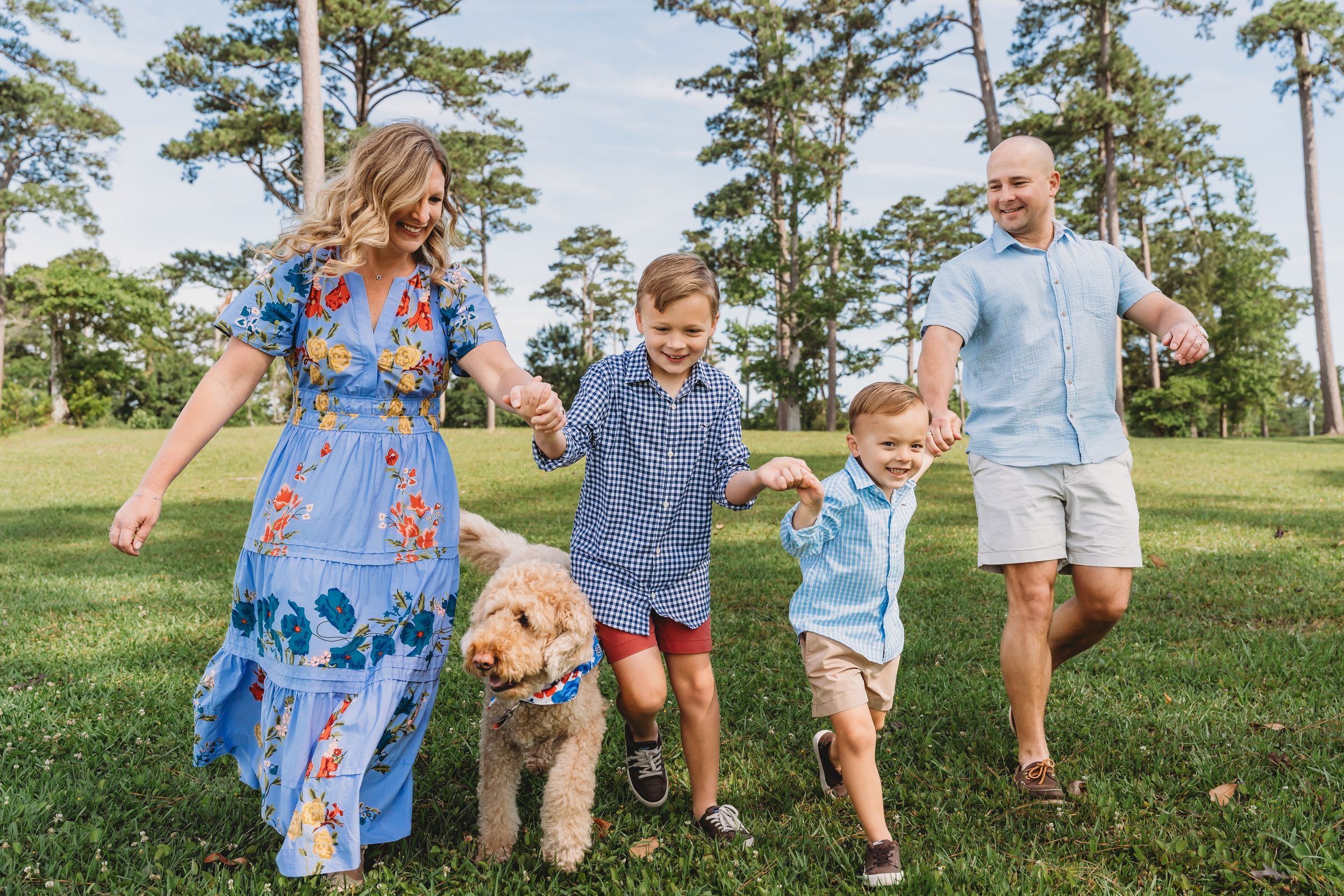 Happy family with two boys and a golden doodle dog playing outdoors in a lush green park on a sunny day.